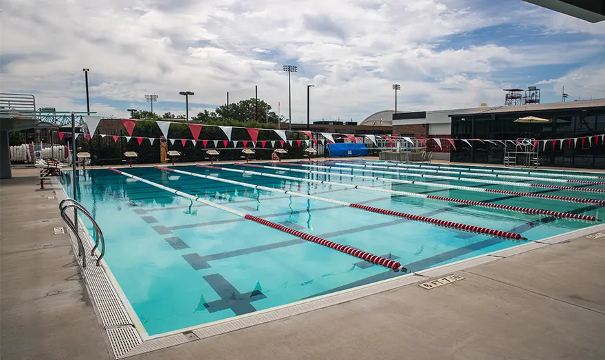 An outdoor pool with red and white pennate flags over the pool. The pool features red and white floating lane lines.