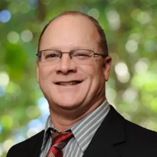 Professional headshot of a man wearing glasses, dressed in business attire, smiling at the camera.