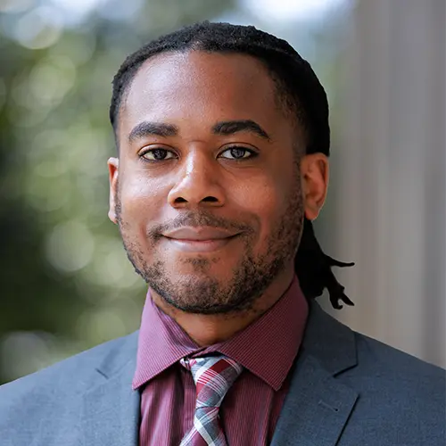 A man dressed in a gray suite in front of a green background.